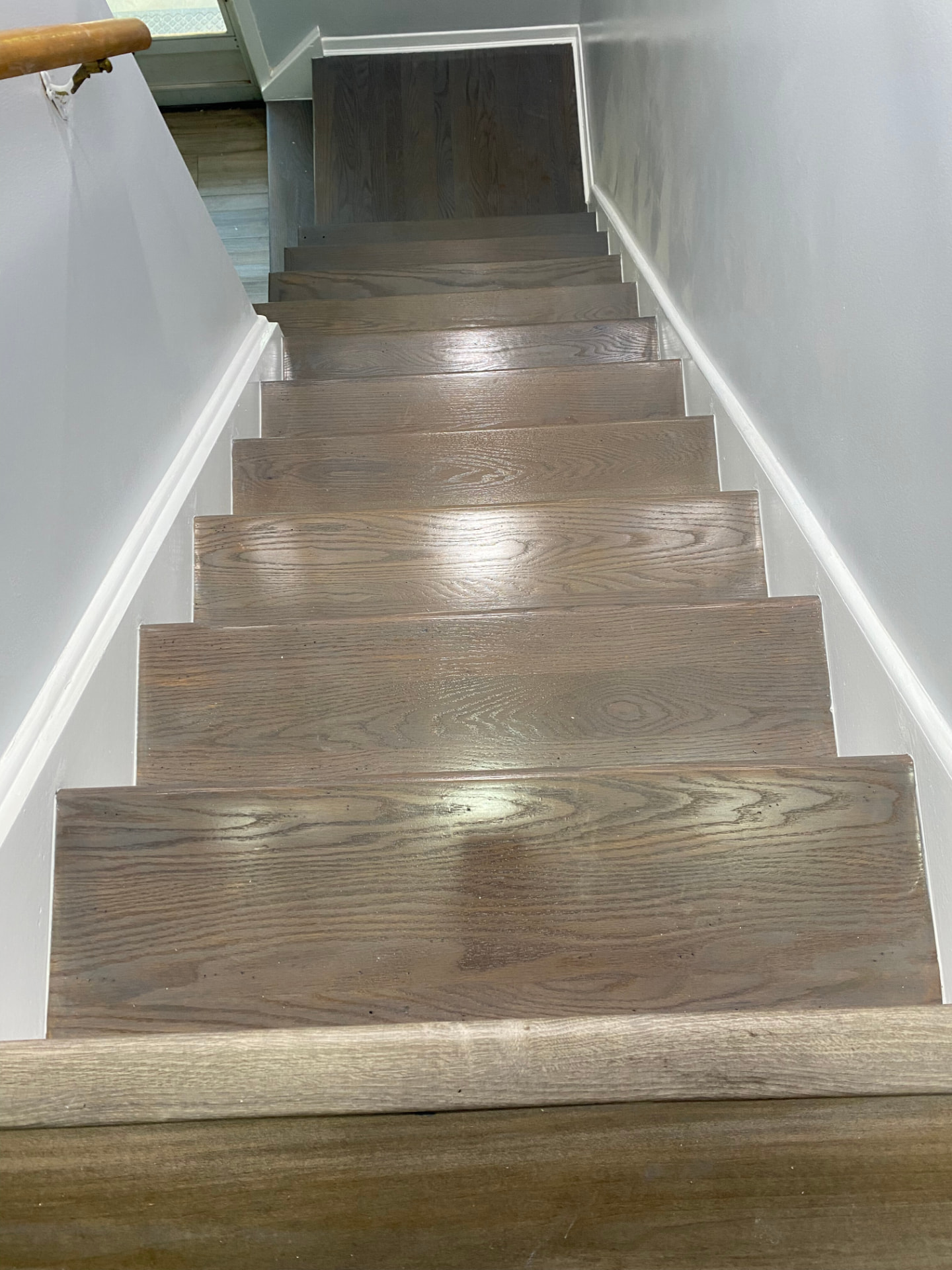 Same stairway with finished wood steps, light walls, and white baseboards