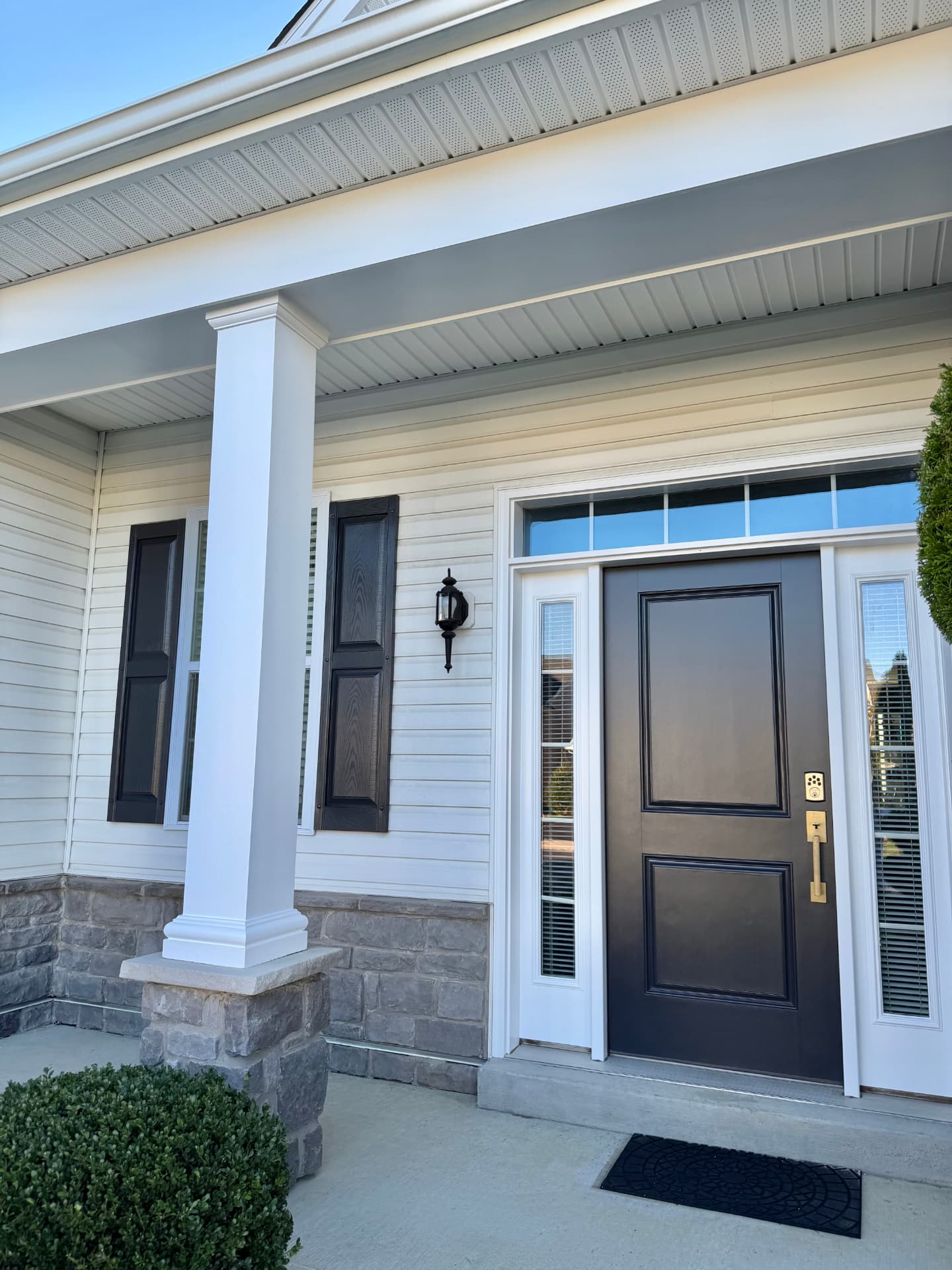 Completed entryway with dark door and shutters beneath white porch trim